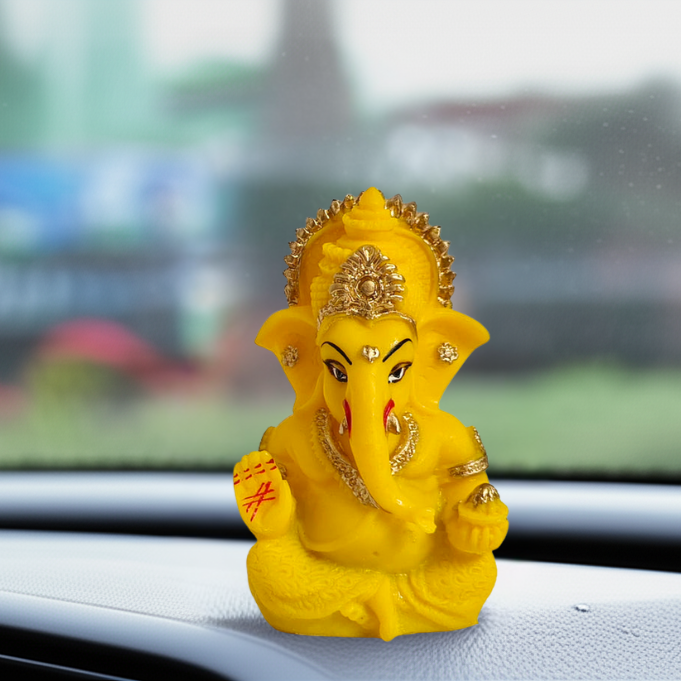 Yellow figurine of Ganesha on a car dashboard with a blurred outdoor background